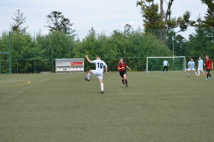 Ein Spieler in einem weißen Trikot mit der Nummer 10 tritt den Ball auf einem Fußballfeld.