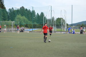 Ein Fußballspieler in rotem Trikot mit der Nummer 4 auf einem Sportplatz mit Kunstrasen.