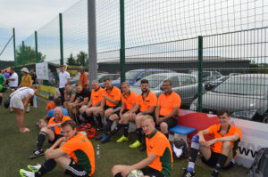 Gruppe von Fußballspielern in orangefarbener Kleidung, die auf einer Bank sitzen und sich ausruhen.
