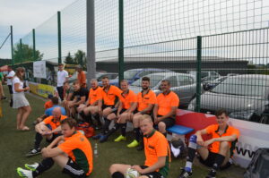 Eine Gruppe von Fußballspielern in orangefarbener Sportkleidung sitzt auf einer Bank am Spielfeldrand.