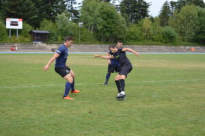 Zwei Fußballspieler in blauen und schwarzen Trikots, die auf einem Rasenfeld spielen.
