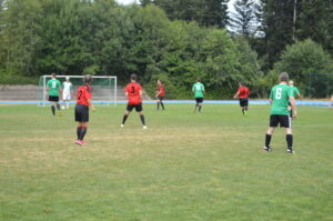 Fußballspiel mit Spielern in roten und grünen Trikots auf einem Rasenplatz.