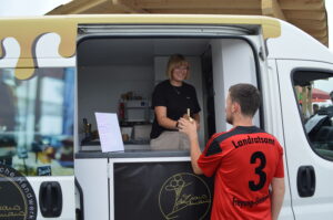 Verkäuferin in einem Eiswagen überreicht einem Kunden ein Eis in einem Becher.