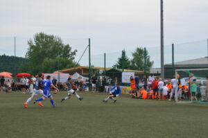 Zwei Fußballspieler in Aktion auf einem Spielfeld, während Zuschauer am Rand stehen.