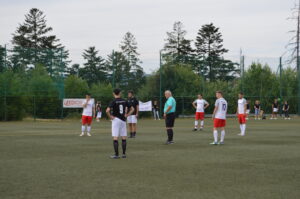Fußballspieler in Schwarz und Weiß stehen auf dem Spielfeld vor einem Schiedsrichter und bereiten sich auf das Spiel vor.