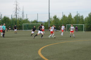 Spieler in weißen und roten Trikots, die auf einem Kunstrasenplatz Fußball spielen.