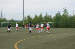 Fünf Spieler in Fußballtrikots spielen auf einem Kunstrasenplatz während eines Spiels.