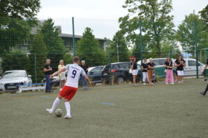 Ein Fußballspieler mit der Nummer 9 schießt auf das Tor während eines Spiels auf einem Sportplatz.