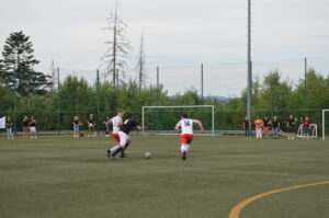 Zwei Fußballspieler in weißen und roten Trikots, die auf einem Kunstrasenplatz gegeneinander antreten.