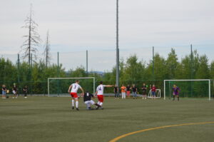 Zwei Fußballspieler in weißen und roten Trikots auf einem Kunstrasenplatz während eines Spiels.