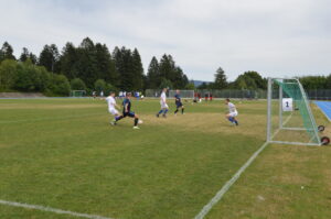 Fußballspiel mit Spielern in weißen und blauen Trikots auf einem Rasenplatz.