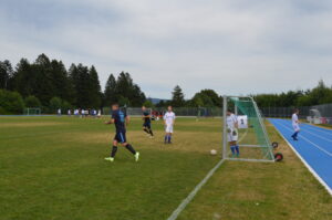 Spieler in blauen und weißen Trikots auf einem Fußballfeld mit einem Tor im Vordergrund.