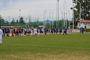 Ein Spieler führt einen Schuss auf einem Fußballfeld aus, während Zuschauer am Rand stehen.