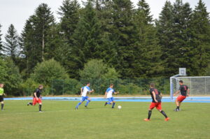 Zwei Spieler in blauen Trikots dribbeln den Ball während eines Fußballspiels gegen Spieler in roten Trikots.