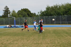 Gruppe von Spielern, die ein Fußballspiel auf einem Sportplatz spielen, mit einem Ball in der Luft.