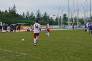 Ein Fußballspieler mit der Nummer 14 in einem weißen Trikot mit roten Shorts, der einen Ball auf einem Spielfeld spielt.