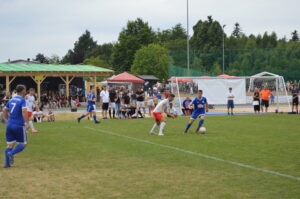 Zwei Fußballspieler, einer in blauem und einer in weißem Trikot, kämpfen um den Ball auf einem Spielfeld.