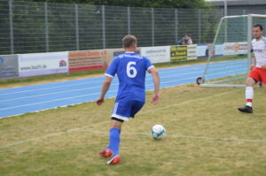 Fußballspieler in blauer Uniform mit der Nummer 6, der den Ball auf einem Spielfeld führt.