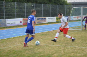 Zwei Fußballspieler auf dem Spielfeld, einer in blauer und der andere in roter Kleidung.