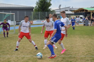 Vier Fußballspieler auf dem Spielfeld, zwei in roten Trikots und zwei in blauen Trikots, während eines Spiels.
