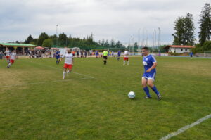 Ein Spieler in blauer Uniform dribbelt den Ball auf einem Fußballfeld während eines Spiels.