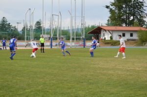 Zwei Fußballspieler in blauen Trikots und einer in einem weißen Trikot auf dem Spielfeld.
