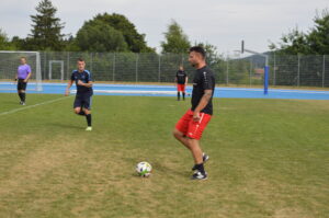 Ein Fußballspieler in roter Shorts und schwarzem Shirt spielt auf einem grünen Spielfeld mit einem Ball.