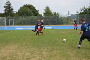 Zwei Fußballspieler in blauen und roten Trikots kämpfen um den Ball auf einem Spielfeld.