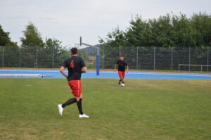 Zwei Fußballspieler in schwarzer und roter Sportkleidung auf einem grünen Spielfeld mit einem Ball.
