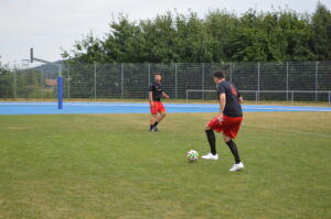 Zwei Fußballspieler in roten Trikots auf einem grünen Spielfeld während des Trainings.
