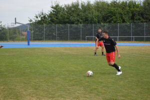 Ein Fußballspieler in schwarzem Trikot und roten Shorts dribbelt den Ball auf einem Trainingsfeld.