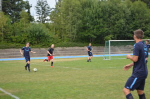 Fußballspieler in blauen Trikots und ein Spieler in rotem Trikot beim Training auf dem Sportplatz.