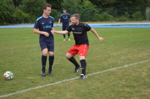 Zwei Fußballspieler, einer in blauem Trikot und der andere in schwarzem und rotem Trikot, während des Trainings auf dem Feld.