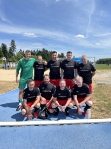 Eine Gruppe von Fußballspielern in schwarzen und roten Trikots posiert auf einem Sportplatz.