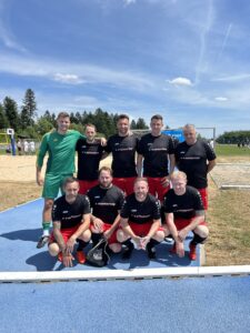 Eine Fußballmannschaft in schwarzen und roten Trikots posiert für ein Gruppenfoto auf einem Sportplatz.