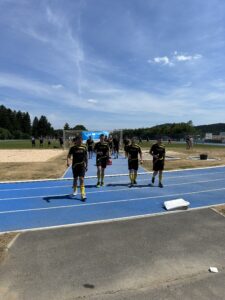 Vier Spieler einer Fußballmannschaft in gelben Socken gehen auf einem blauen Laufbahnweg zum Spielfeld.