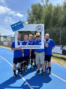 Sechs Fußballspieler posieren zusammen mit einem Rahmen auf einem Sportplatz.