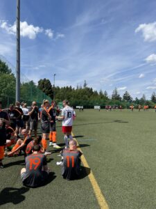 Fußballspieler in grauen und orangefarbenen Trikots auf einem Sportplatz während eines Spiels.