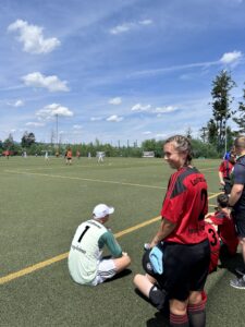 Fußballspiel mit einer Spielerin in rotem Trikot, die auf dem Spielfeld sitzt und zuschaut.