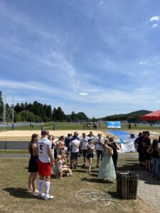 Eine Gruppe von Menschen versammelt sich bei einer Sportveranstaltung im Freien, umgeben von Sportplätzen und Bäumen.