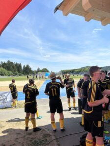 Gruppe von Fußballspielern in schwarzen Trikots mit gelben Akzenten, die auf ein Spielfeld schauen.