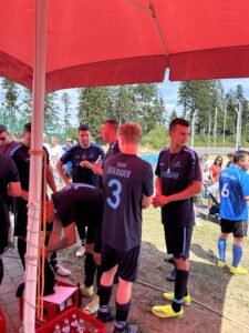 Fußballmannschaft in blauen Trikots mit Namen auf dem Rücken, die sich unter einem roten Zelt versammelt.