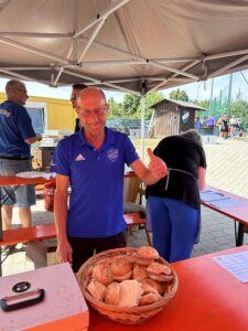 Ein Mann in einem blauen Shirt zeigt einen Daumen hoch neben einem Korb mit Brötchen.