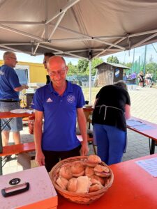 Ein Mann in blauem Shirt steht an einem Verkaufsstand mit einem Korb voller Brötchen.