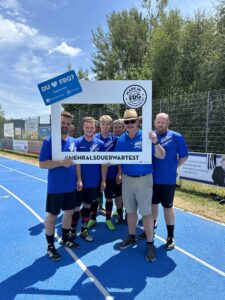 Sechs Fußballspieler posieren zusammen mit einem großen Rahmen auf einem Sportplatz.