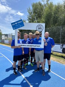 Sechs Fußballspieler posieren mit einem großen Rahmen auf einem Sportplatz.