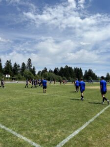 Gruppen von Spielern in blauen und schwarzen Trikots auf einem Fußballfeld unter einem bewölkten Himmel.