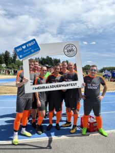 Gruppe von Fußballspielern, die einen Rahmen mit dem Text '#MEHRALSDUERWARTEST' halten.