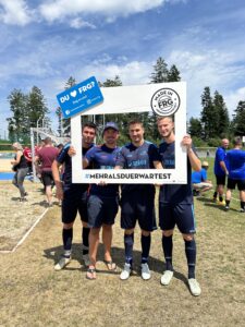 Vier Fußballspieler posieren mit einem großen Rahmen, der den Text '#MEHRALSDUERWARTEST' enthält.