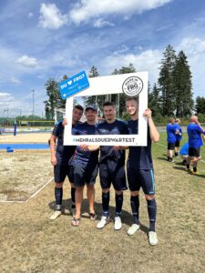 Vier Personen posieren mit einem großen Rahmen auf einem Sportplatz während eines Events.